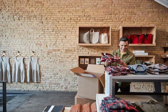 Smiling man in a fashion store packing shirts in boxes for a clothing order