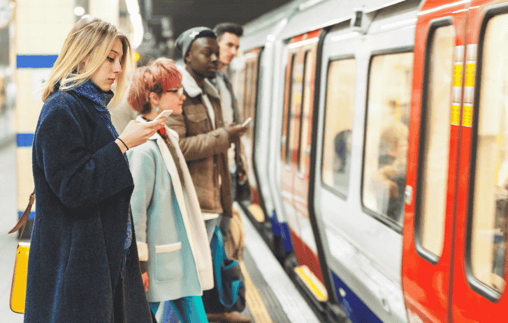 Personnes qui attendent sur un quai de métro près d’une rame, l’une d’elles consulte son téléphone.