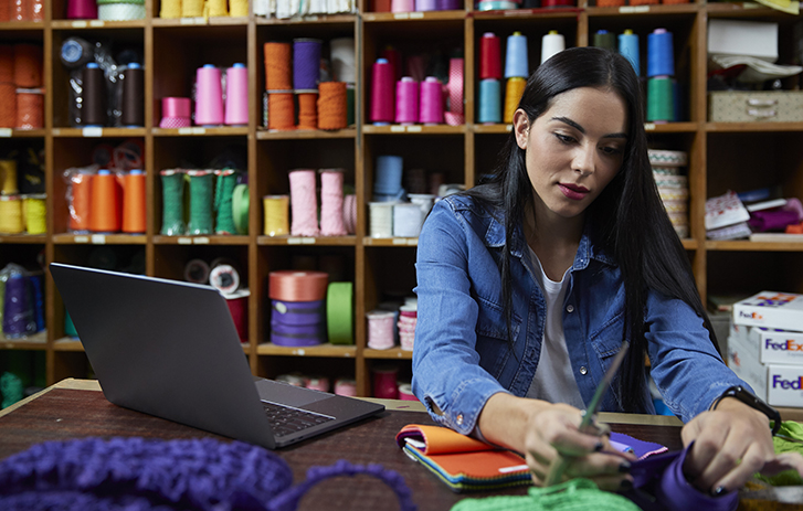 Woman looking at a spool of yarn with a laptop beside her