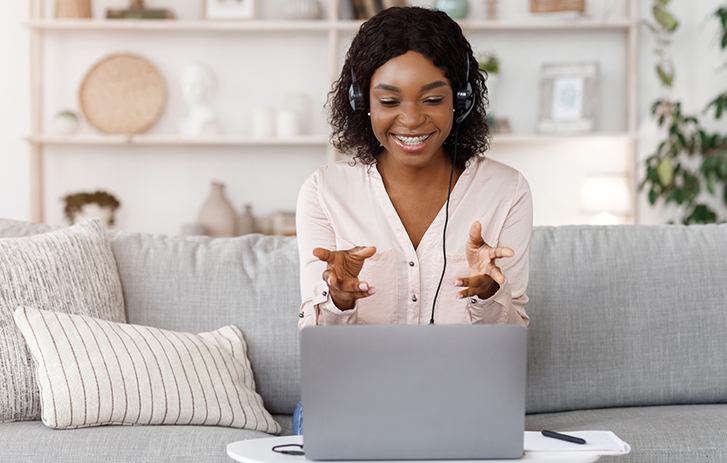 Person on a couch with headphones smiling down at their laptop