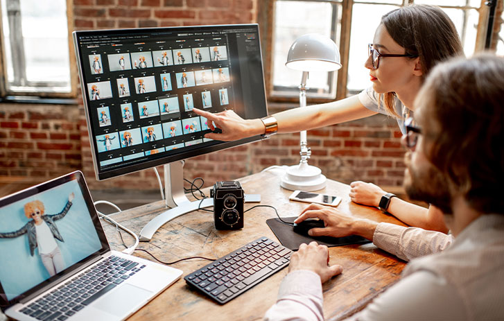 Man and woman working on a portrait design on two computer at desk 