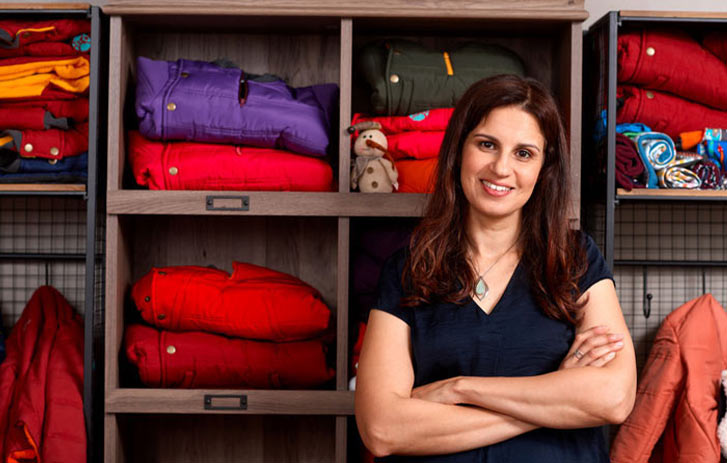 A photo of Dahlia Rizk, founder of Buckle Me Baby Coats, standing in front of a display of coats