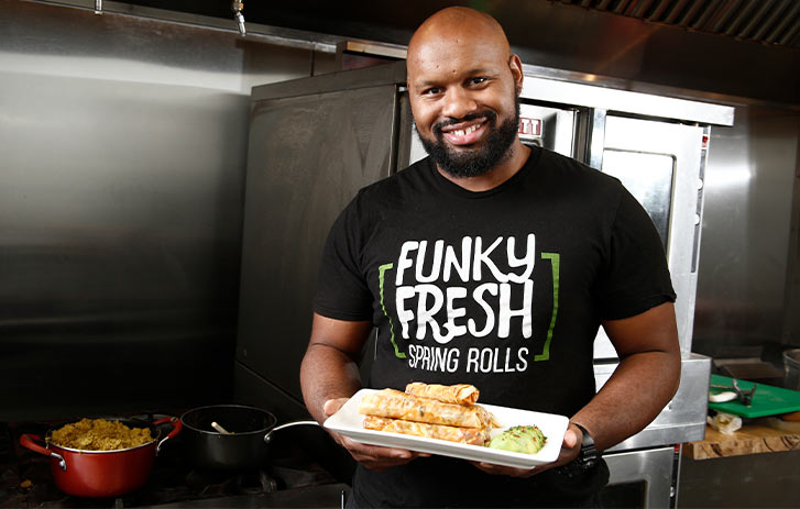 A photo of Funky Fresh Spring Rolls founder Trueman McGee holding a platter of rolls in a kitchen