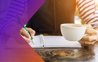 A close-up of a person holding a coffee cup in front of an open notebook.