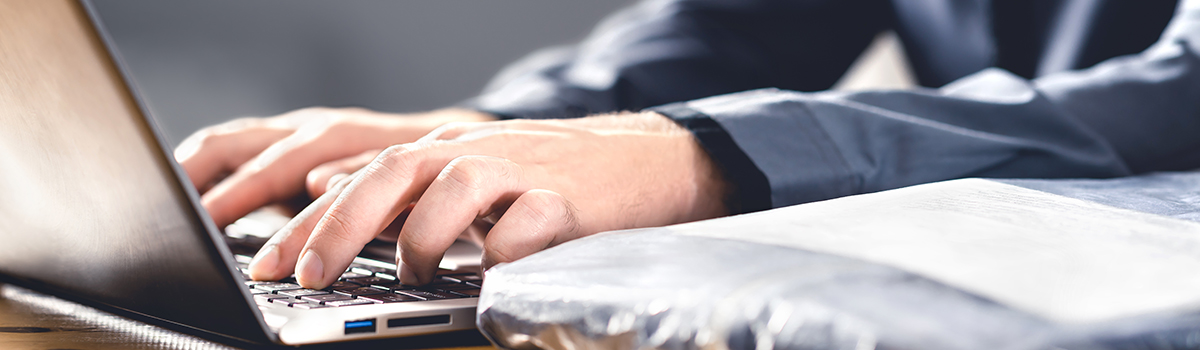 Close-up of hands typing on a laptop with a package nearby