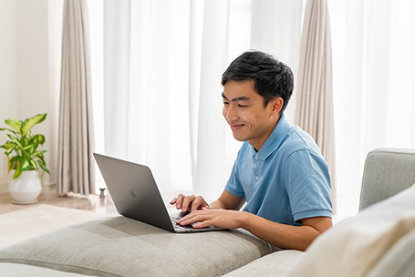 Person in a blue shirt using a laptop computer while on a sofa