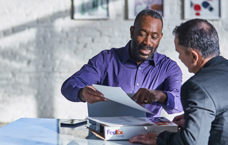 businessmen reviewing documents over white fedex box