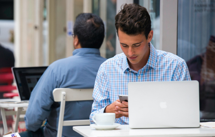 man sitting outside coffee shop while looking at his cell phone