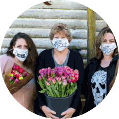 Three women wearing facemasks while they hold an assortment of flowers