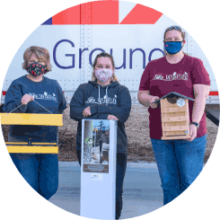 Three women wearing facemasks while holding different types of birdhouses