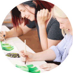 Two women smiling as they work on painted art