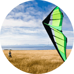 A person standing in a field of tall grass while flying a green kite