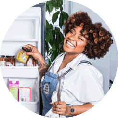 A woman smiling as she’s grabbing something from a refrigerator door