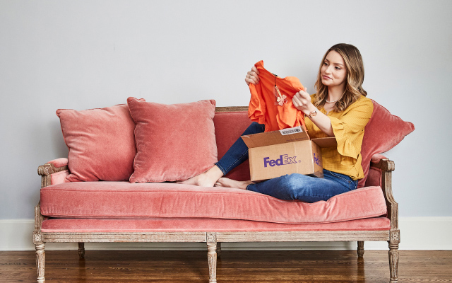 A woman sitting on a love seat holding an orange shirt.