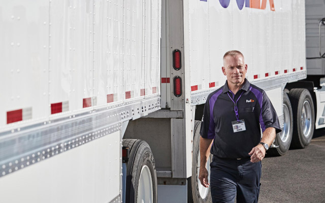 Courier walks near FedEx trucks to deliver packages