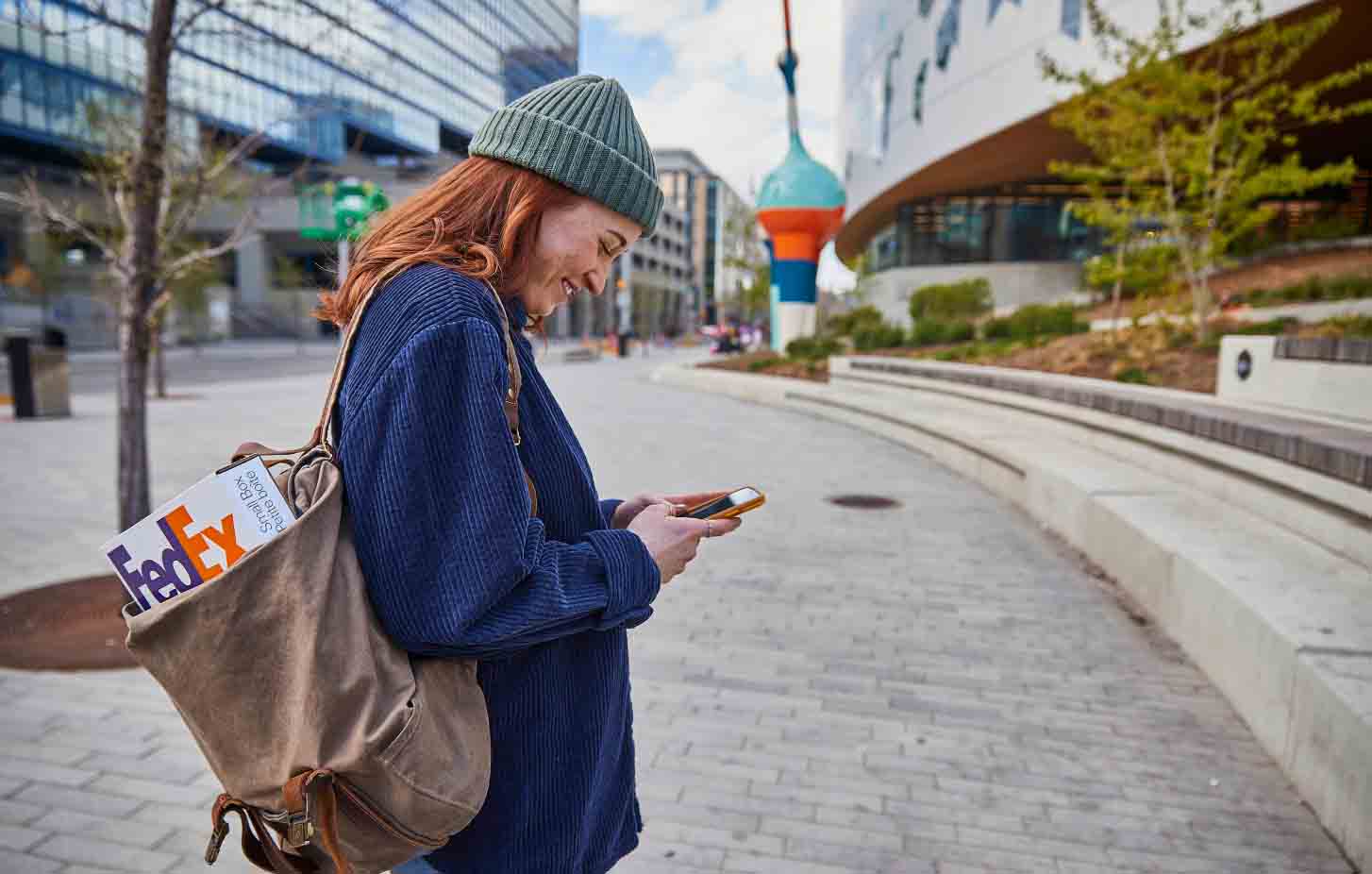 A woman looking at her phone with a FedEx package in her bag.