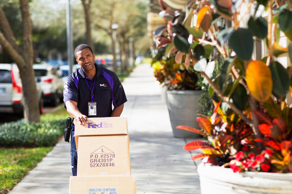 A FedEx team member uses a dolly to bring packages across the street.