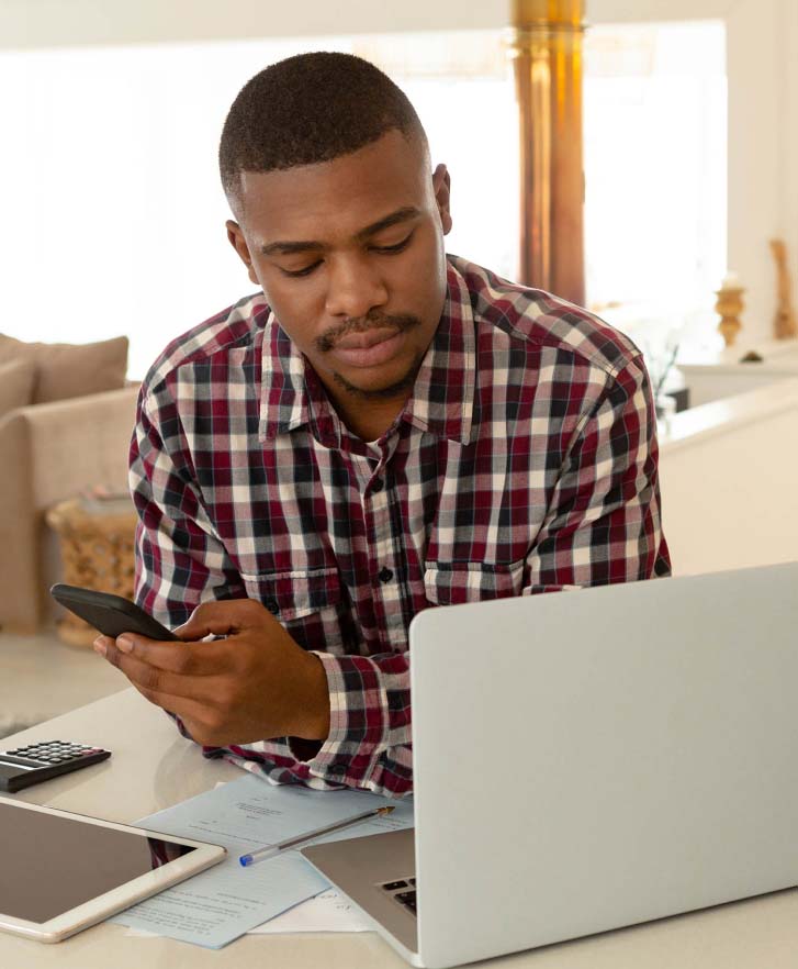 Man referencing a laptop while using his mobile phone