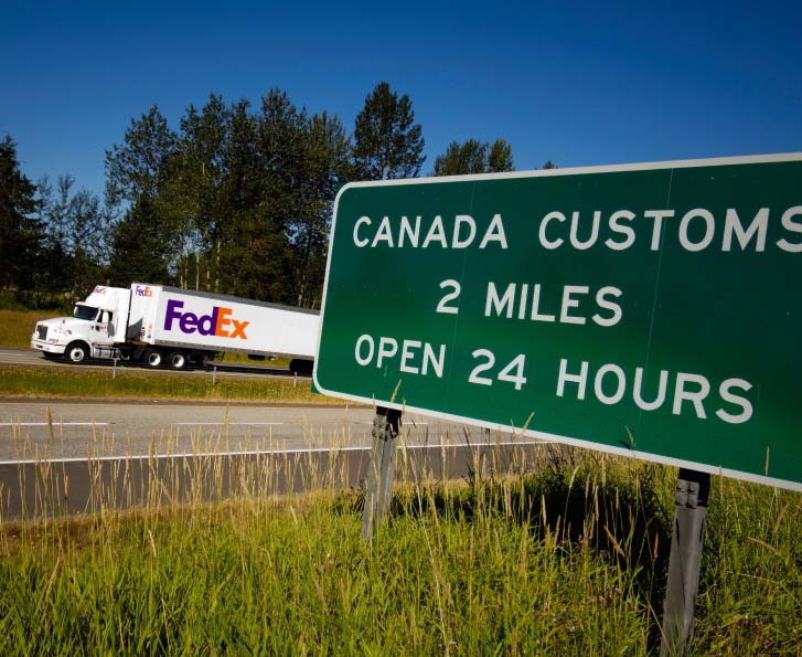 FedEx freight truck driving on the highway next to a Canadian Customs sign